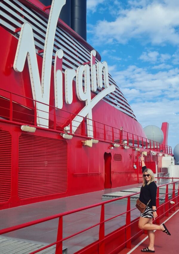 Gallivanting Laura standing by the Virgin Voyages logo on board the Valiant Lady